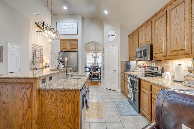 kitchen featuring arched walkways, light stone counters, a sink, appliances with stainless steel finishes, and decorative light fixtures