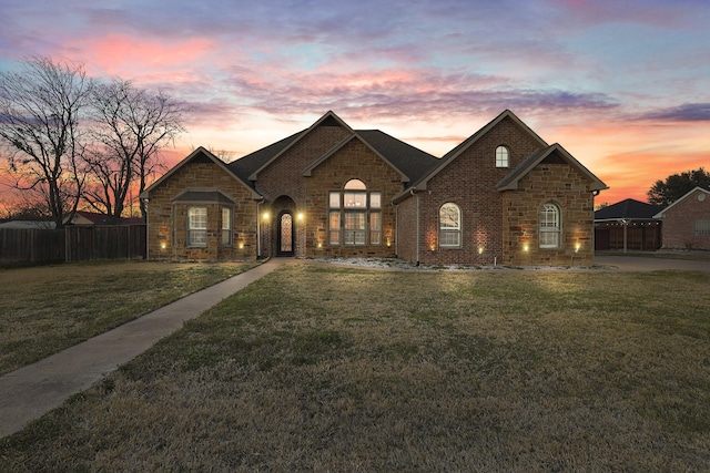 french country style house with a front lawn, fence, and brick siding