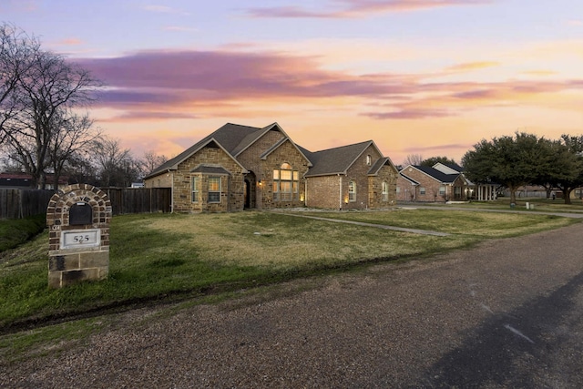 french country style house featuring stone siding, fence, and a lawn