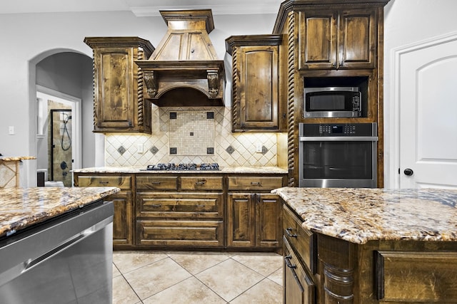 kitchen featuring tasteful backsplash, ornamental molding, light stone countertops, stainless steel appliances, and premium range hood