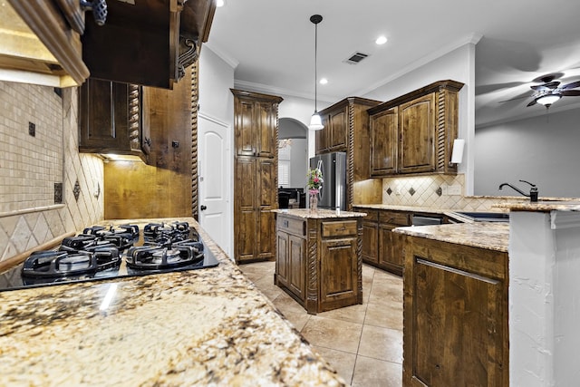 kitchen with arched walkways, a kitchen island, freestanding refrigerator, a sink, and black gas stovetop