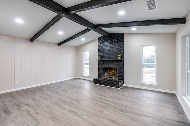 unfurnished living room with vaulted ceiling with beams, visible vents, a brick fireplace, wood finished floors, and baseboards