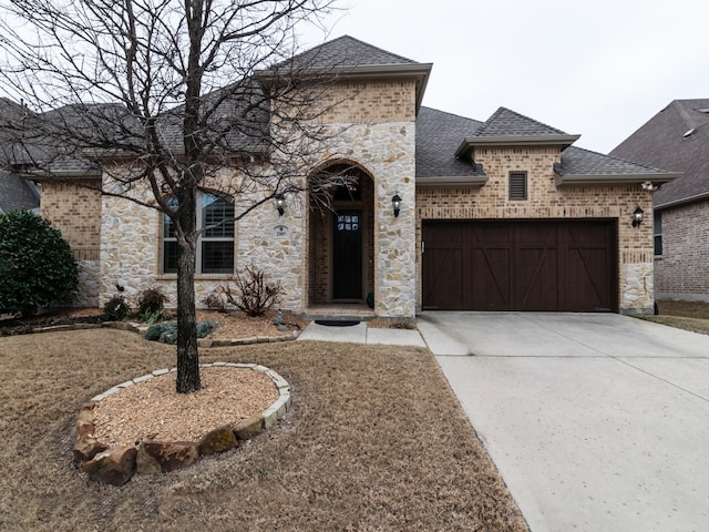 french country style house featuring a garage, a shingled roof, brick siding, concrete driveway, and stone siding