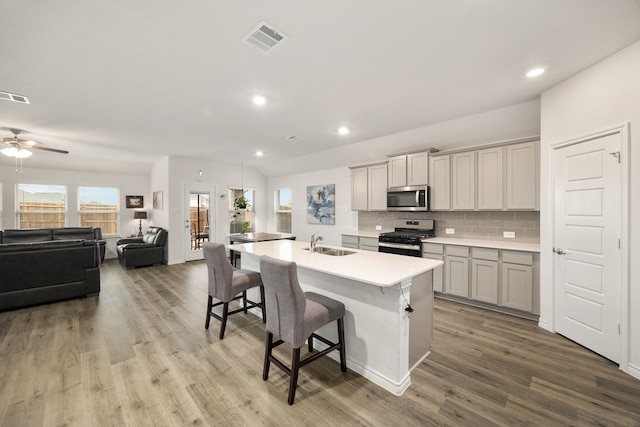 kitchen with visible vents, a center island with sink, a sink, stainless steel appliances, and a breakfast bar area