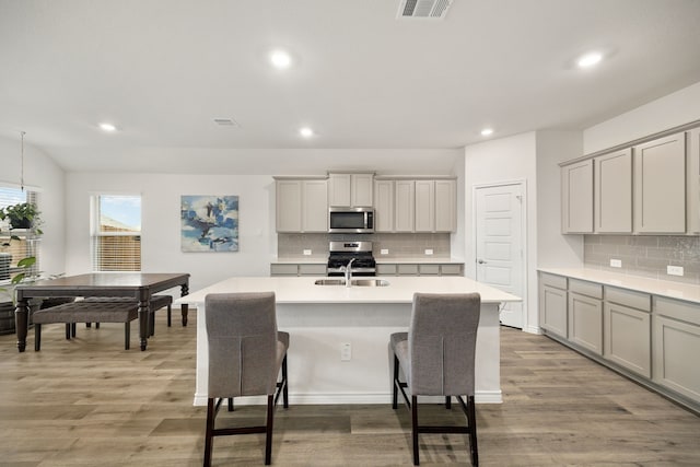 kitchen featuring visible vents, an island with sink, appliances with stainless steel finishes, light wood-type flooring, and a sink