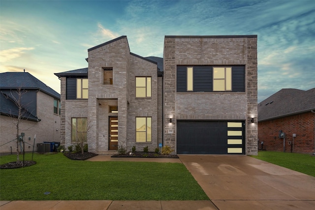 contemporary home with central AC unit, concrete driveway, an attached garage, a yard, and brick siding