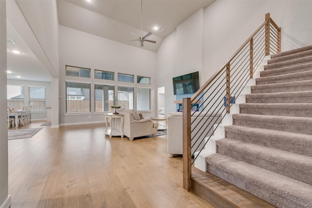 entrance foyer with ceiling fan, high vaulted ceiling, light wood-style flooring, baseboards, and stairs