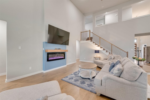 living room featuring visible vents, stairway, a glass covered fireplace, wood finished floors, and baseboards