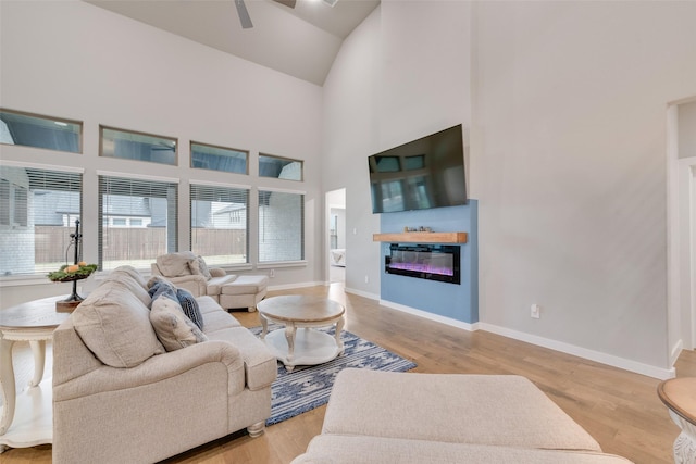 living area featuring high vaulted ceiling, light wood finished floors, a glass covered fireplace, and baseboards