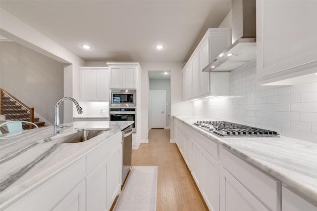 kitchen with wall chimney exhaust hood, a sink, white cabinetry, and stainless steel appliances