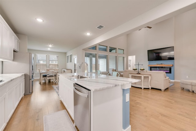 kitchen featuring visible vents, an island with sink, stainless steel appliances, white cabinetry, and a sink