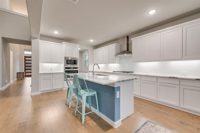 kitchen featuring wall chimney exhaust hood, a center island with sink, white cabinetry, and stainless steel appliances