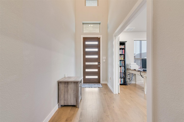 entryway with light wood-style floors, a textured wall, and baseboards