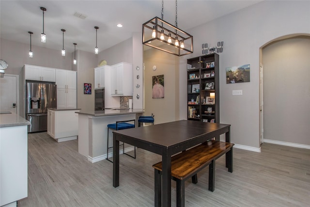 dining room featuring light wood-style floors, visible vents, arched walkways, and baseboards