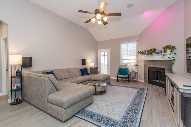 living area with light wood-style floors, lofted ceiling, a tiled fireplace, and a ceiling fan