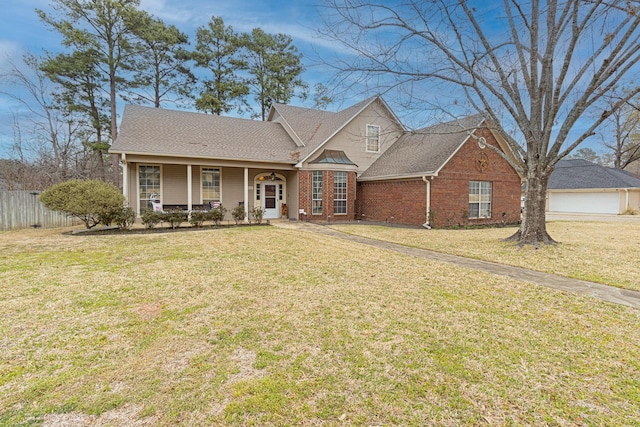 traditional-style home with covered porch, brick siding, a shingled roof, fence, and a front yard