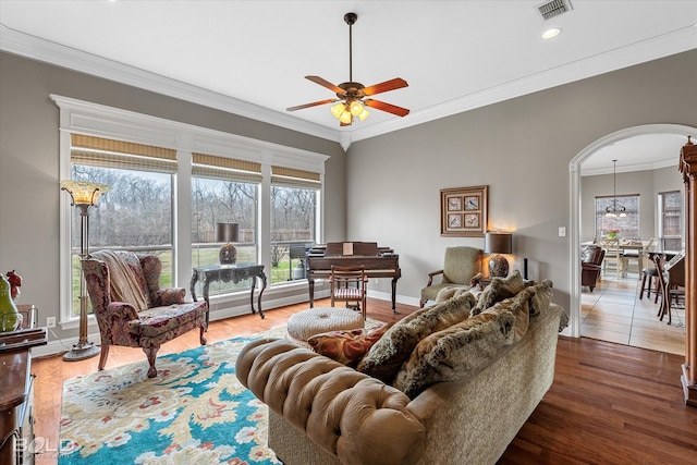 living area with arched walkways, a baseboard radiator, visible vents, ornamental molding, and wood finished floors