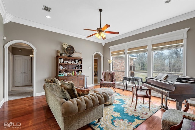 living room with dark wood-style floors, arched walkways, visible vents, and ornamental molding