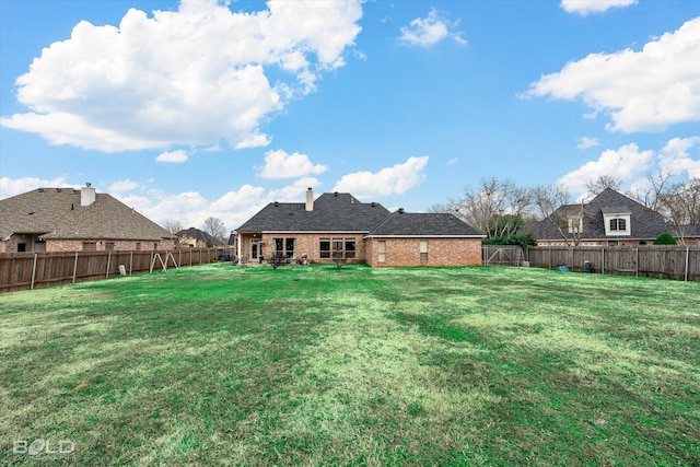 back of house with a yard, brick siding, and a fenced backyard