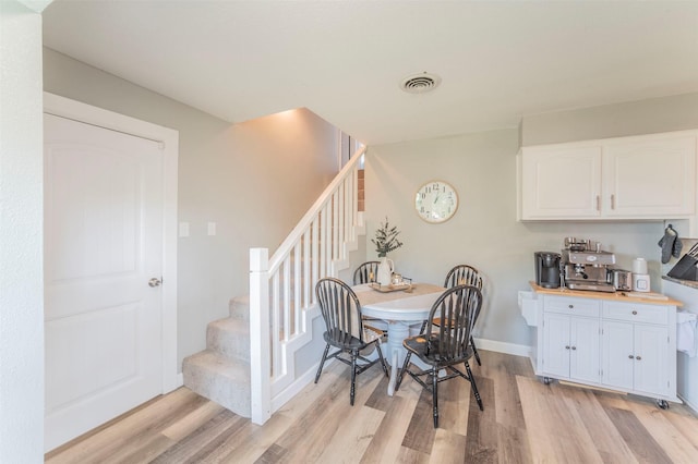 dining room with light wood-style floors, baseboards, stairs, and visible vents