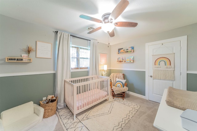 bedroom featuring visible vents, light colored carpet, a ceiling fan, a crib, and baseboards