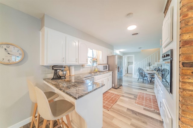 kitchen featuring visible vents, dark stone countertops, a peninsula, stainless steel appliances, and white cabinetry