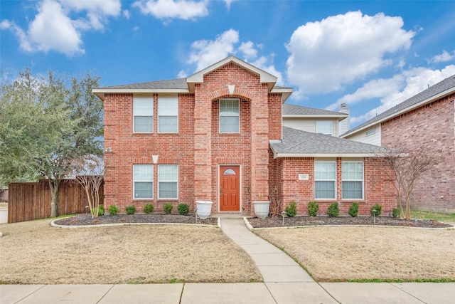 traditional-style home with brick siding, roof with shingles, a front yard, and fence