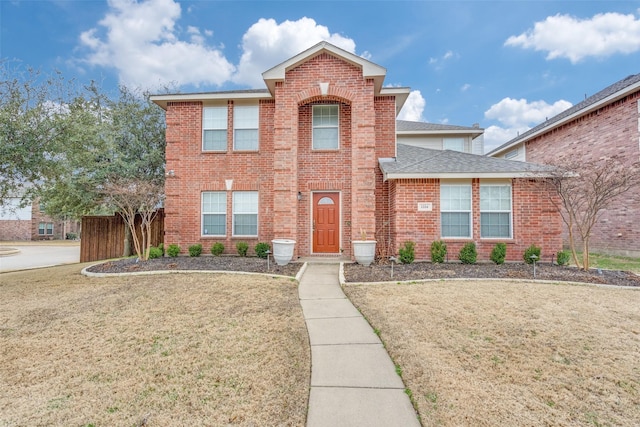 traditional-style home with brick siding, a front lawn, a shingled roof, and fence