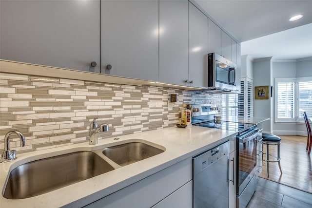 kitchen with stainless steel appliances, light countertops, decorative backsplash, a sink, and modern cabinets