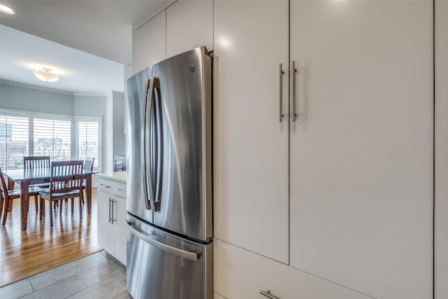 kitchen featuring light countertops, ornamental molding, freestanding refrigerator, white cabinets, and light tile patterned flooring