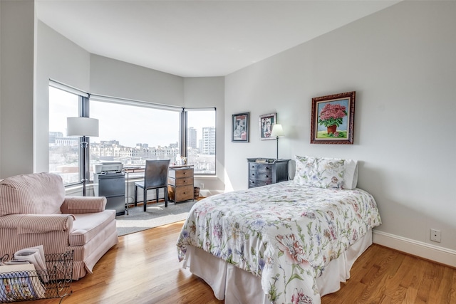 bedroom with a city view, baseboards, and wood finished floors