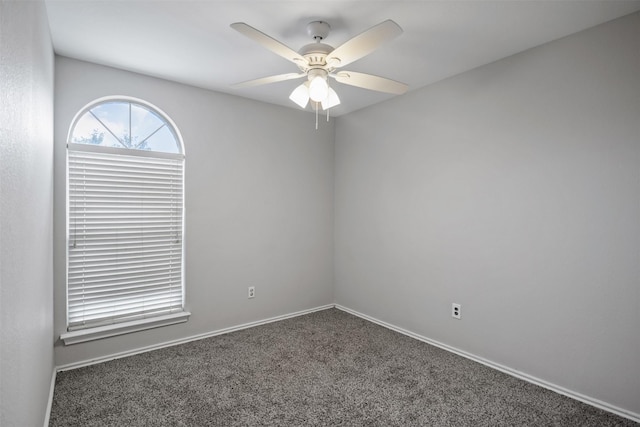 spare room featuring ceiling fan, dark carpet, and baseboards