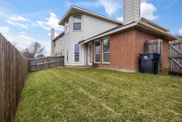 rear view of house featuring a fenced backyard, brick siding, a chimney, and a lawn