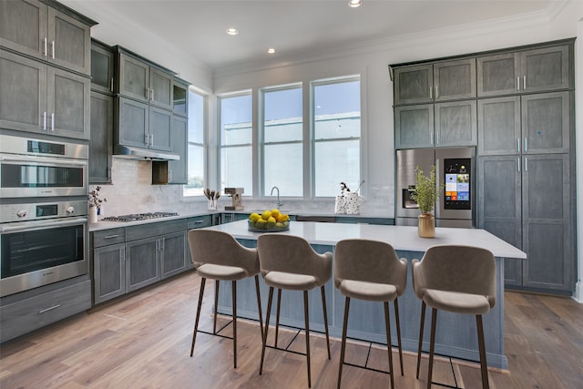 kitchen featuring crown molding, stainless steel appliances, light countertops, a kitchen island, and a kitchen bar