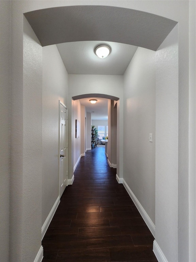 hallway with baseboards, arched walkways, and dark wood-style flooring