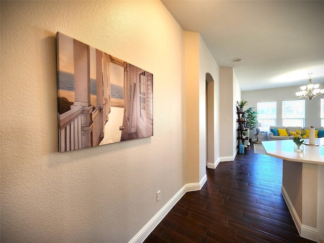 hallway featuring dark wood-style floors, arched walkways, a chandelier, and baseboards