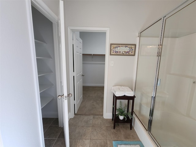 full bathroom with a walk in closet, a shower stall, baseboards, and tile patterned floors