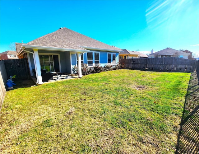 rear view of house featuring roof with shingles, a lawn, a patio area, and a fenced backyard