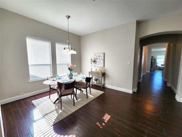 dining space with an inviting chandelier, baseboards, arched walkways, and dark wood-type flooring