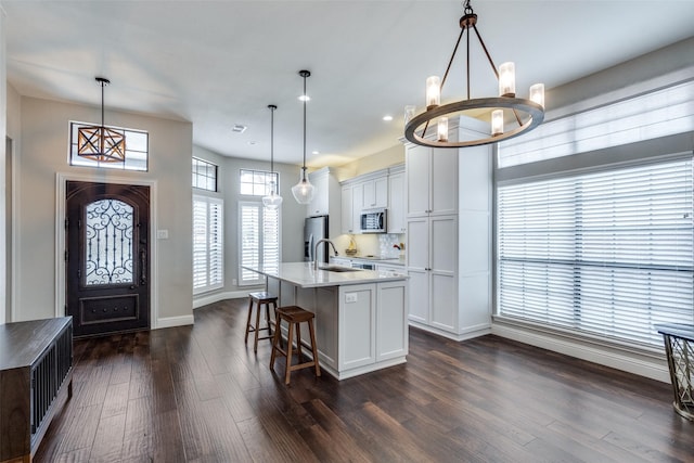 kitchen featuring a chandelier, a kitchen island with sink, stainless steel appliances, white cabinetry, and pendant lighting