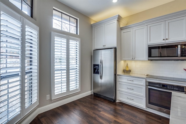 kitchen with light stone counters, stainless steel appliances, dark wood-type flooring, white cabinets, and tasteful backsplash