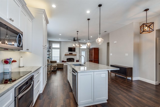 kitchen featuring stainless steel appliances, a sink, white cabinetry, open floor plan, and pendant lighting