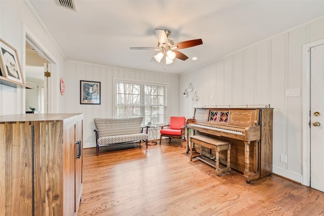 sitting room featuring a ceiling fan, wood finished floors, visible vents, and crown molding