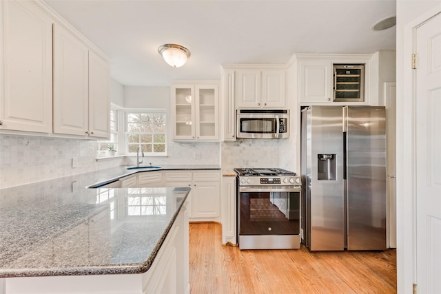 kitchen featuring stone counters, stainless steel appliances, a sink, white cabinetry, and glass insert cabinets