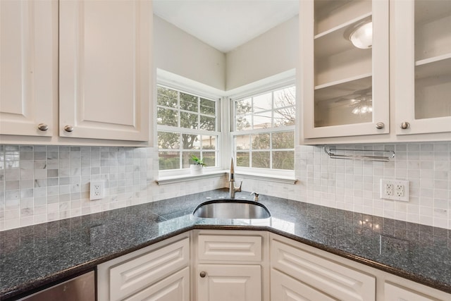 kitchen with dark stone countertops, a sink, glass insert cabinets, and white cabinetry