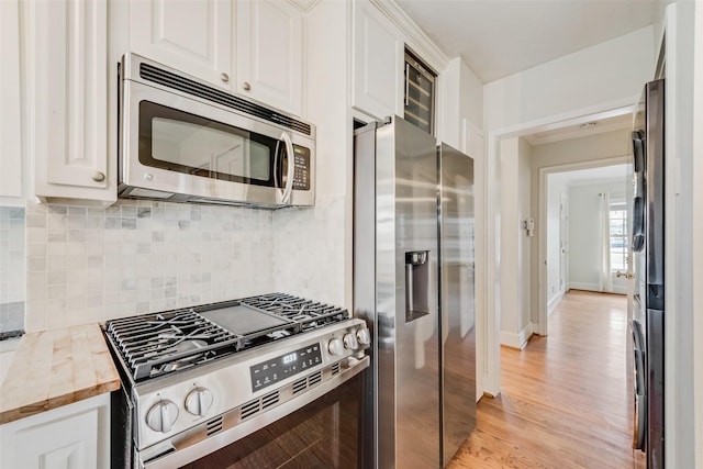 kitchen featuring backsplash, appliances with stainless steel finishes, light wood-style floors, white cabinets, and baseboards