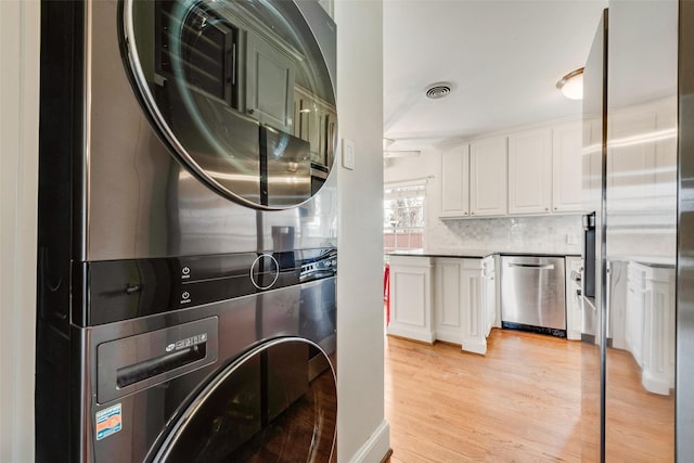 kitchen featuring stacked washer and dryer, visible vents, light wood-type flooring, white cabinetry, and stainless steel dishwasher