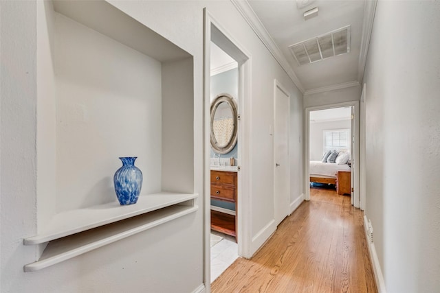 hall featuring light wood-style floors, visible vents, crown molding, and baseboards