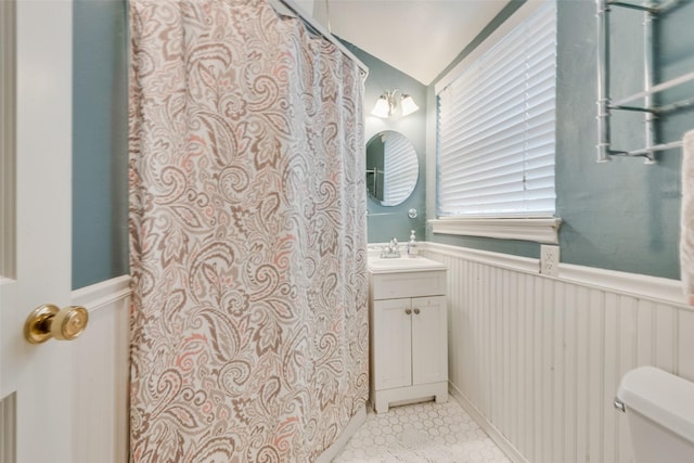 full bathroom featuring a wainscoted wall, vaulted ceiling, vanity, and toilet