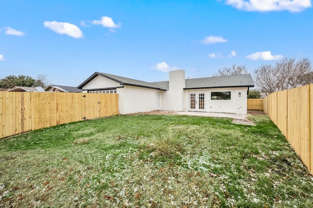 rear view of house featuring a yard, french doors, a fenced backyard, and brick siding